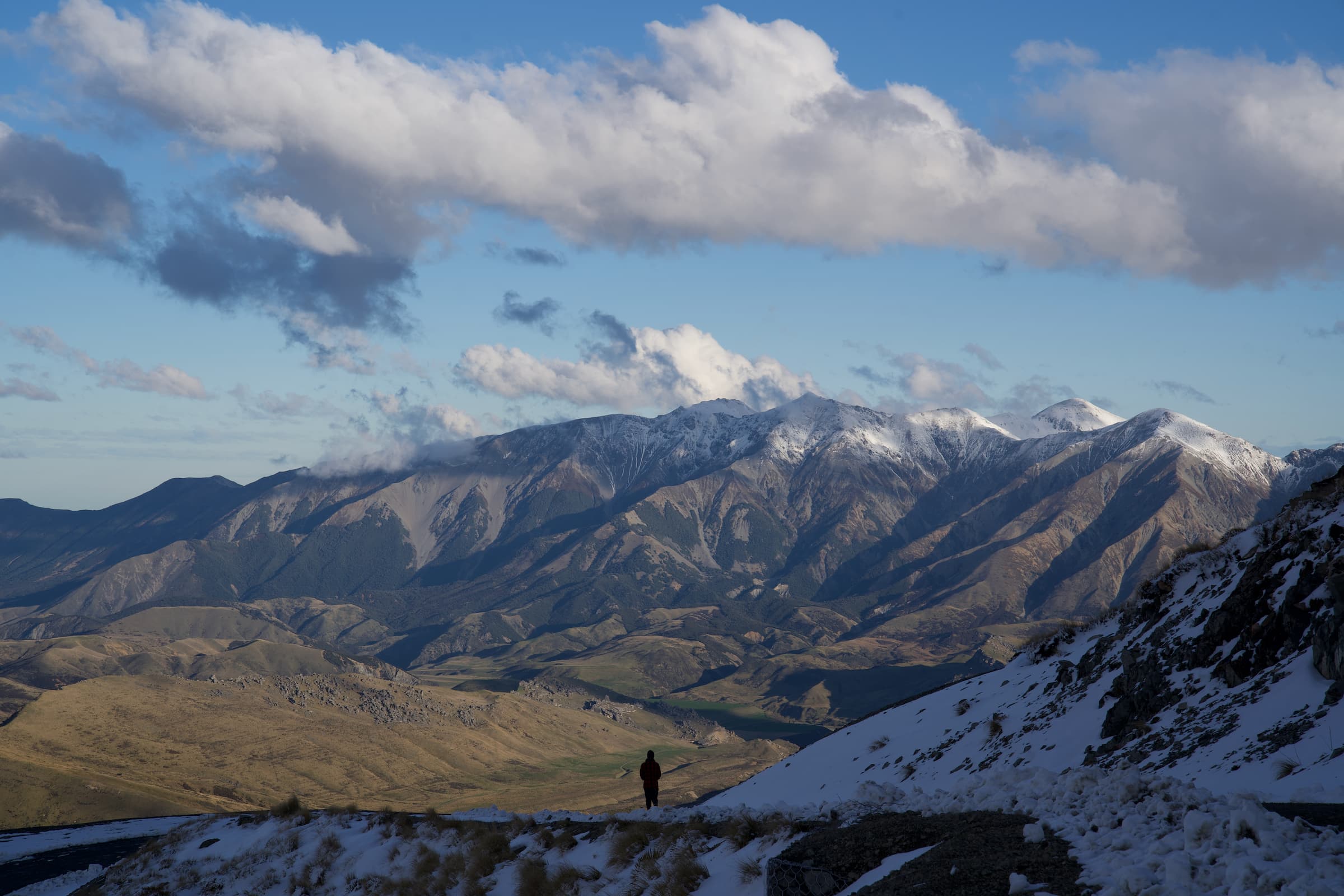 A lone figure walks down a snowy road to see the view into the valley below